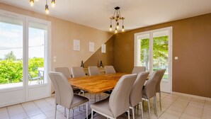 Uma sala de jantar ampla com uma grande mesa de madeira, seis cadeiras e um candelabro.