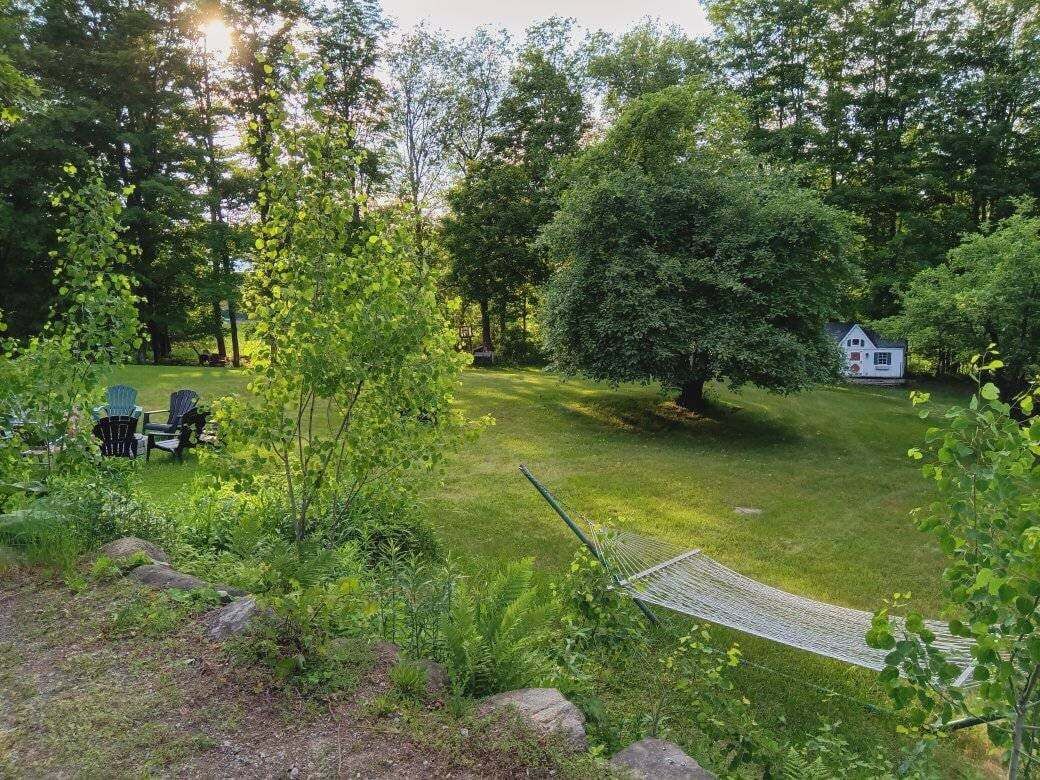 A grassy backyard with a hammock, a small white house, and a gazebo.