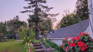 A backyard with a barbecue grill, a flower bed with red flowers, and a staircase leading to a house. - 10 Mi To Gore Mountain: Home In Adirondack Park 5 Bedroom Home (Olmstedville)