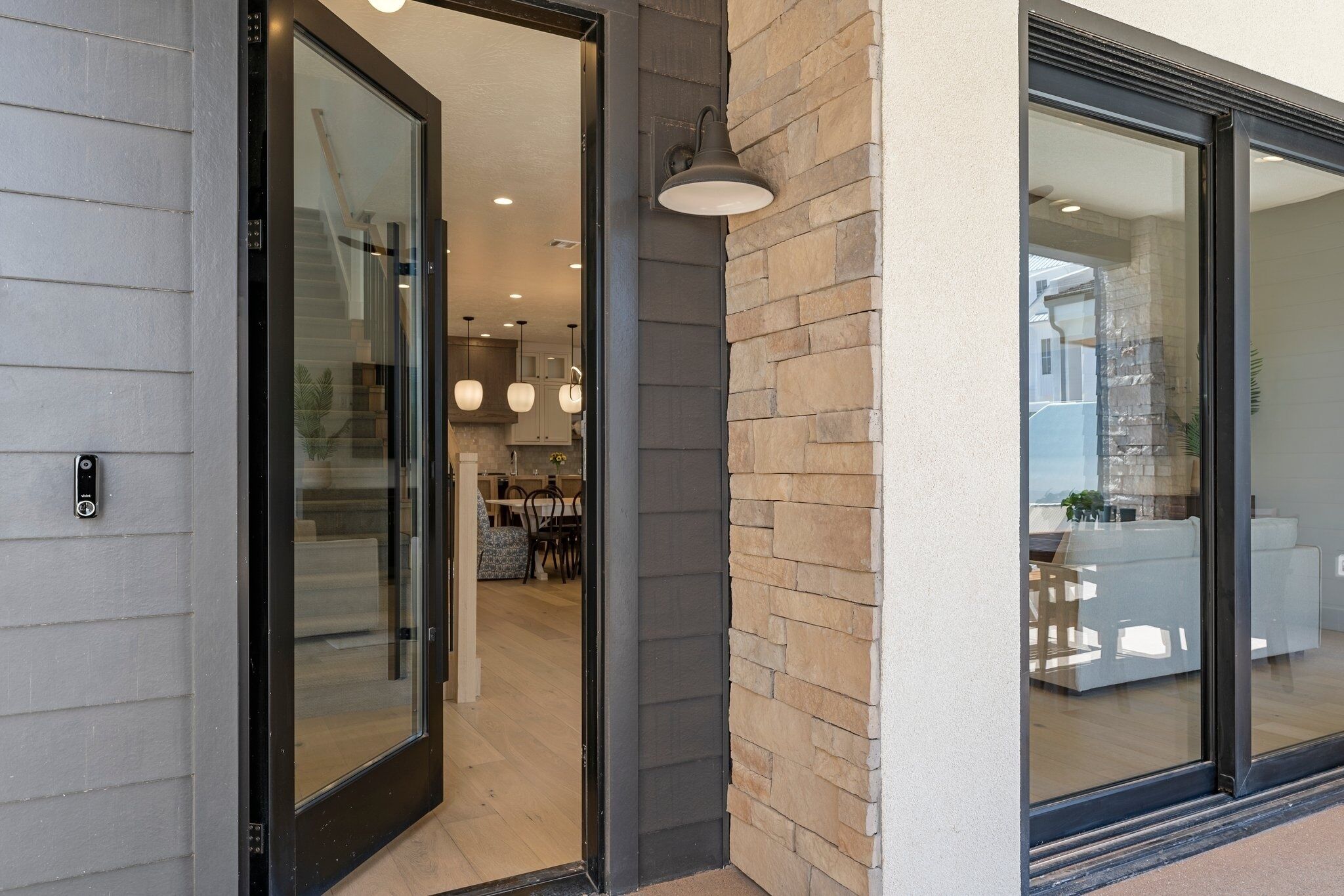 A modern entrance with glass doors, a brick wall, and a visible dining area with a table and chairs.