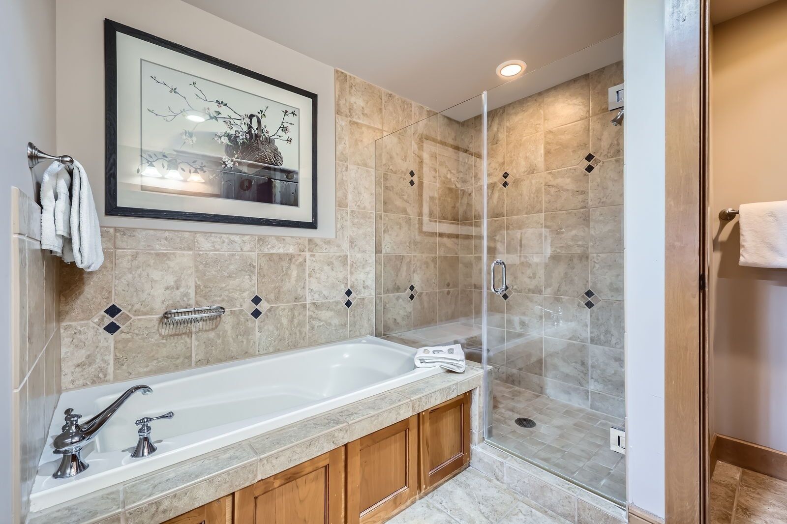 A modern bathroom with a large bathtub, a glass-enclosed shower, and a framed picture above the sink.
