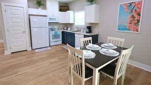 A compact kitchen with white cabinets, a refrigerator, and a dining table set with plates and napkins.