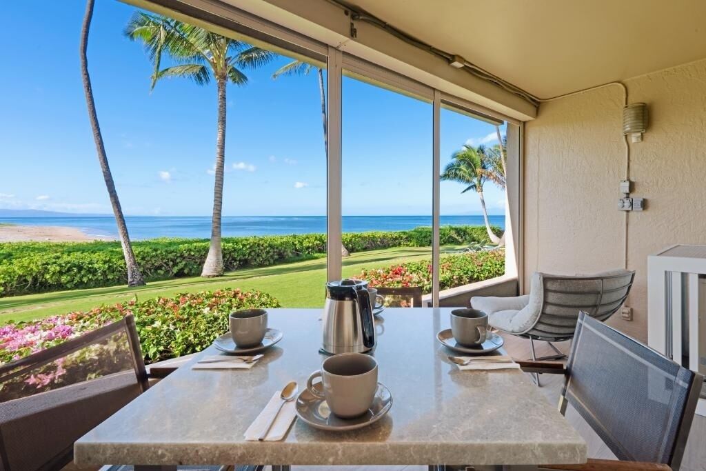 A dining area with a table set for two, overlooking a beach and palm trees.