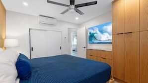 A bedroom with a bed, a ceiling fan, a wardrobe, and a wall-mounted TV. - Menehune Shores, #119 2 Bedroom Condo (Kihei)