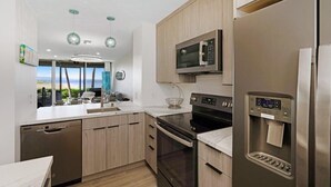 A modern kitchen with a dishwasher, oven, microwave, and water dispenser. - Menehune Shores, #119 2 Bedroom Condo (Kihei)