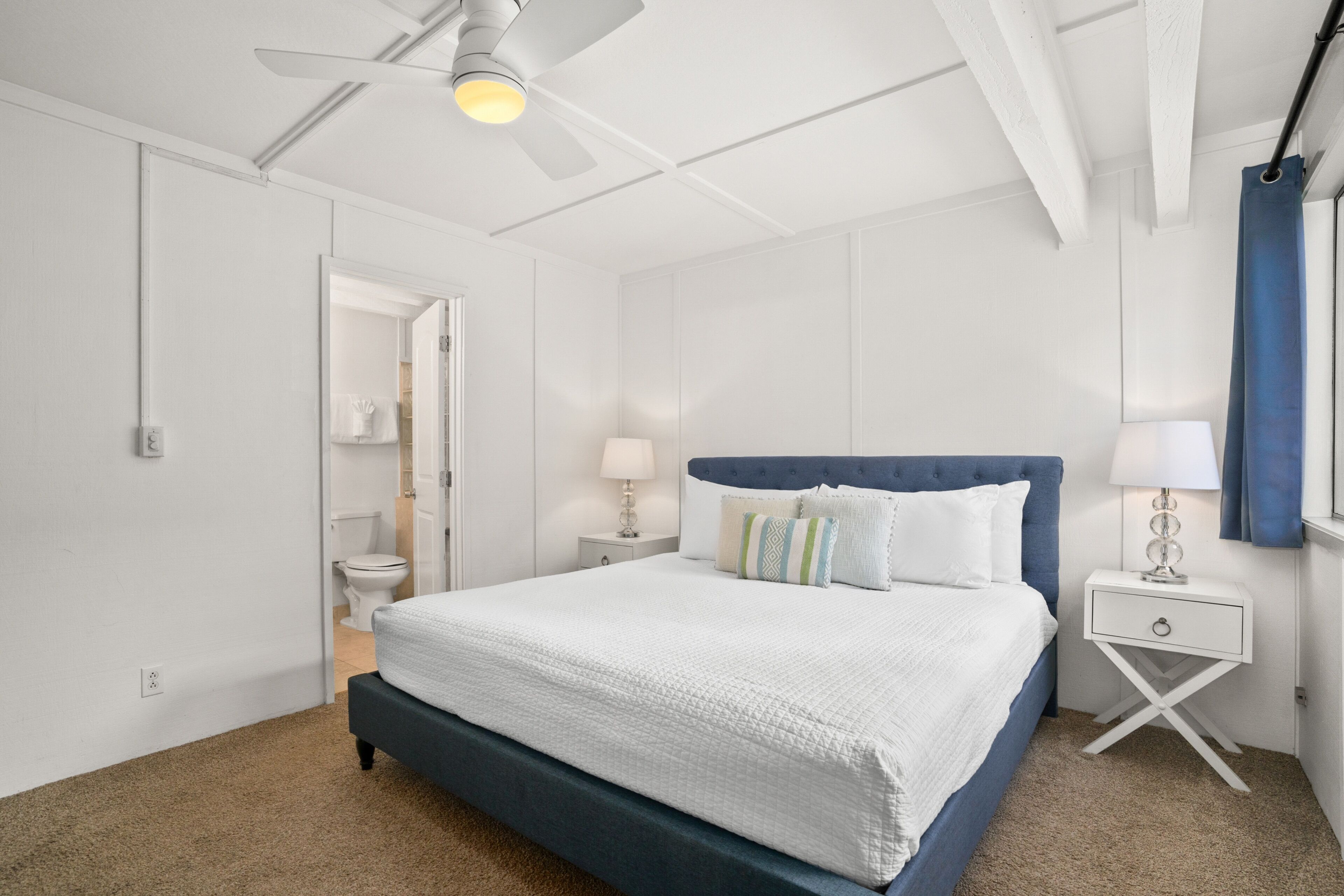 A bedroom with a bed, nightstands, a ceiling fan, and a bathroom visible through an open door.