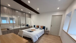 A modern bedroom with a wooden floor, a bed with a white duvet, a small table, and a nightstand with a lamp.