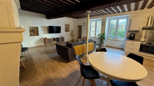 A modern kitchen with a built-in oven, a dining area with a round table and chairs, and a living room with a sofa and a TV.