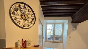 A kitchen with a large wall clock, a window with a view, and a stainless steel sink.