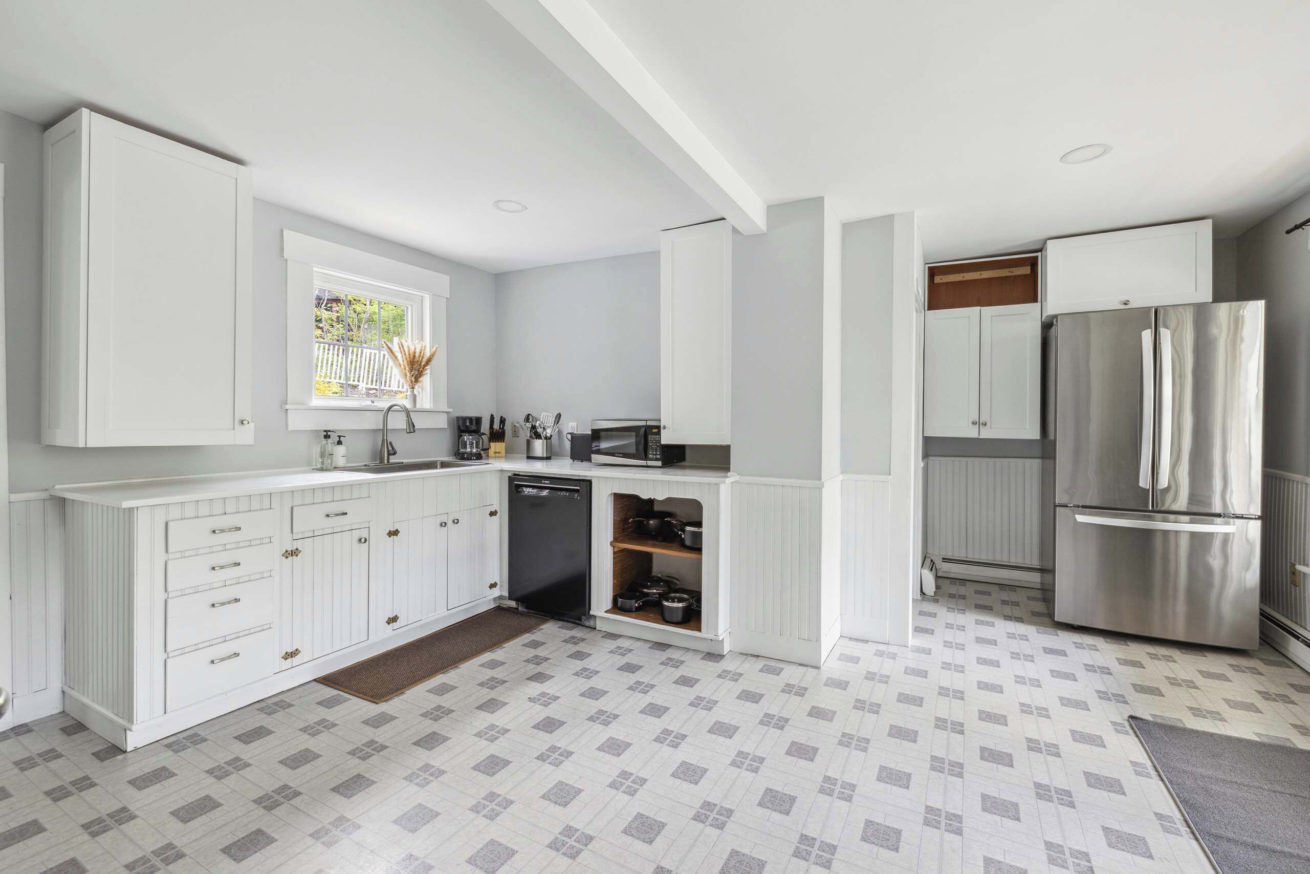 Een moderne keuken met witte kasten, een roestvrijstalen koelkast en een raam met uitzicht op groen.