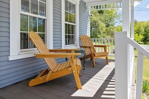 A wooden deck with two Adirondack chairs and a small table.