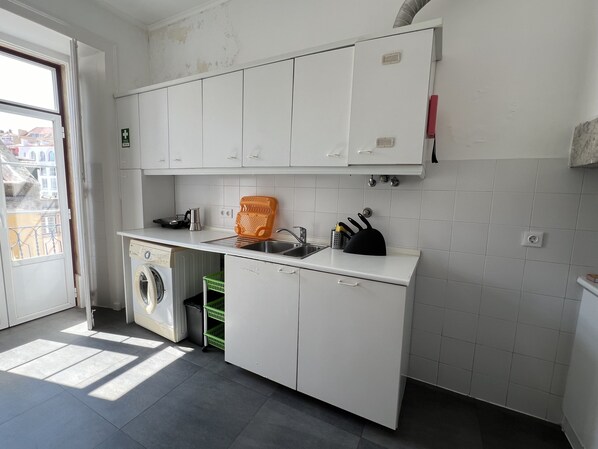 Une cuisine avec des meubles blancs, un lave-linge, un évier et un panier vert.