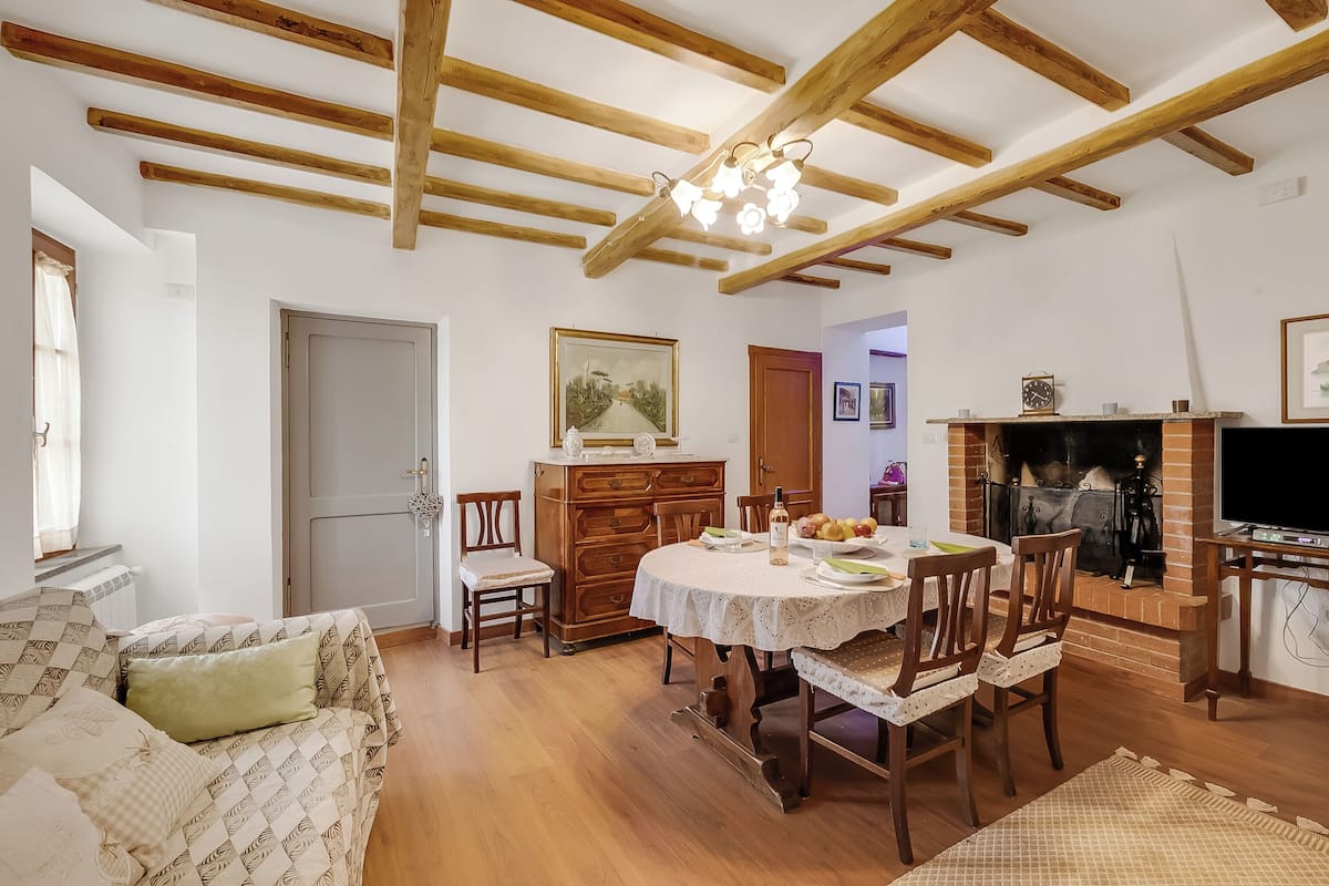 A cozy living room with a wooden ceiling, a dining table with chairs, a sofa, and a fireplace.