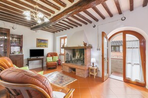 A living room with a fireplace, leather sofa, television, and a view through an open door. - Borgo Panicale Apartments (Panicale)