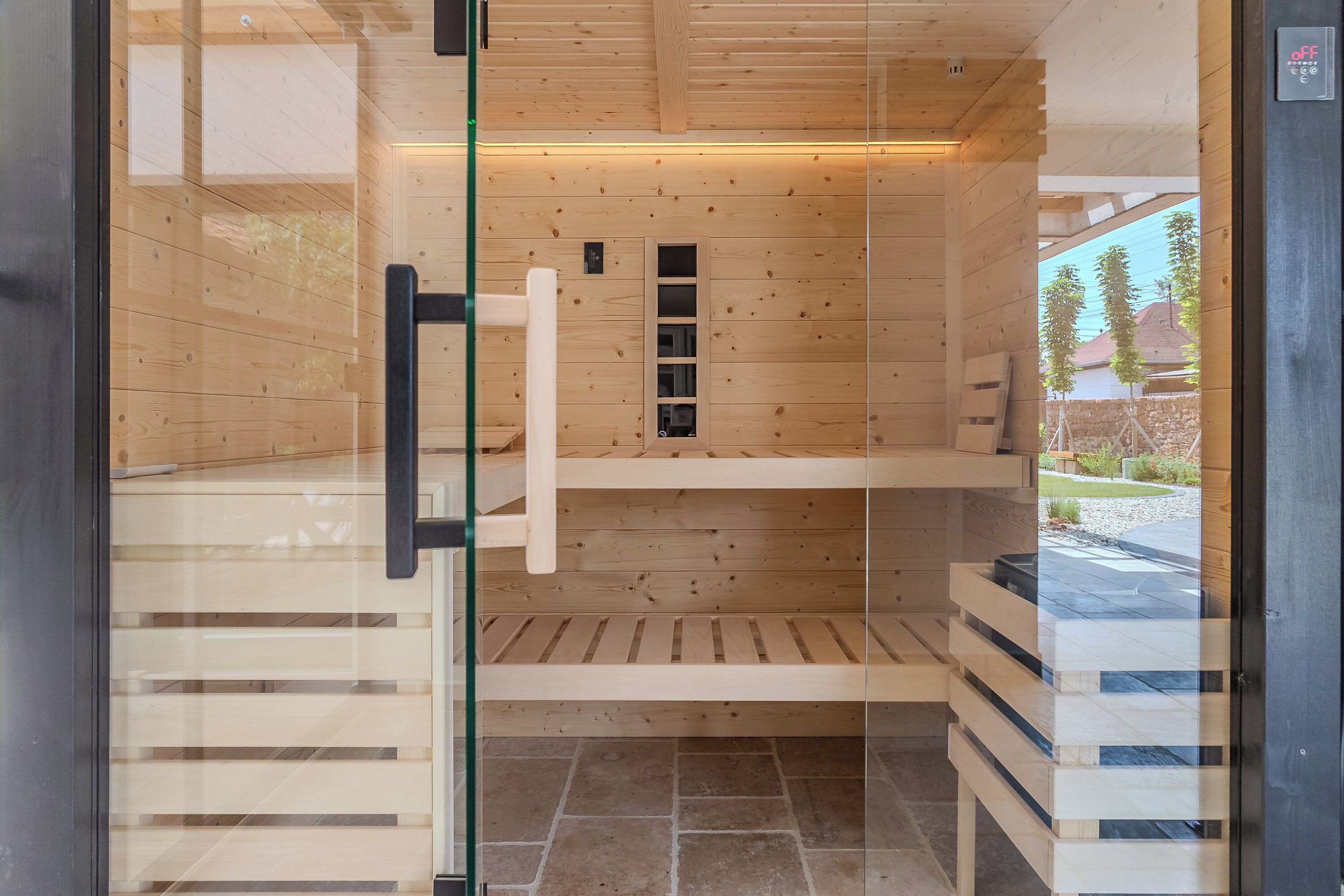 A sauna with wooden walls and a glass door, featuring a bench and shelves.
