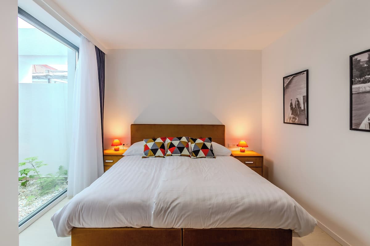Una camera da letto con un letto grande, due lampade ai comodini, una finestra con tende e due quadri appesi al muro.