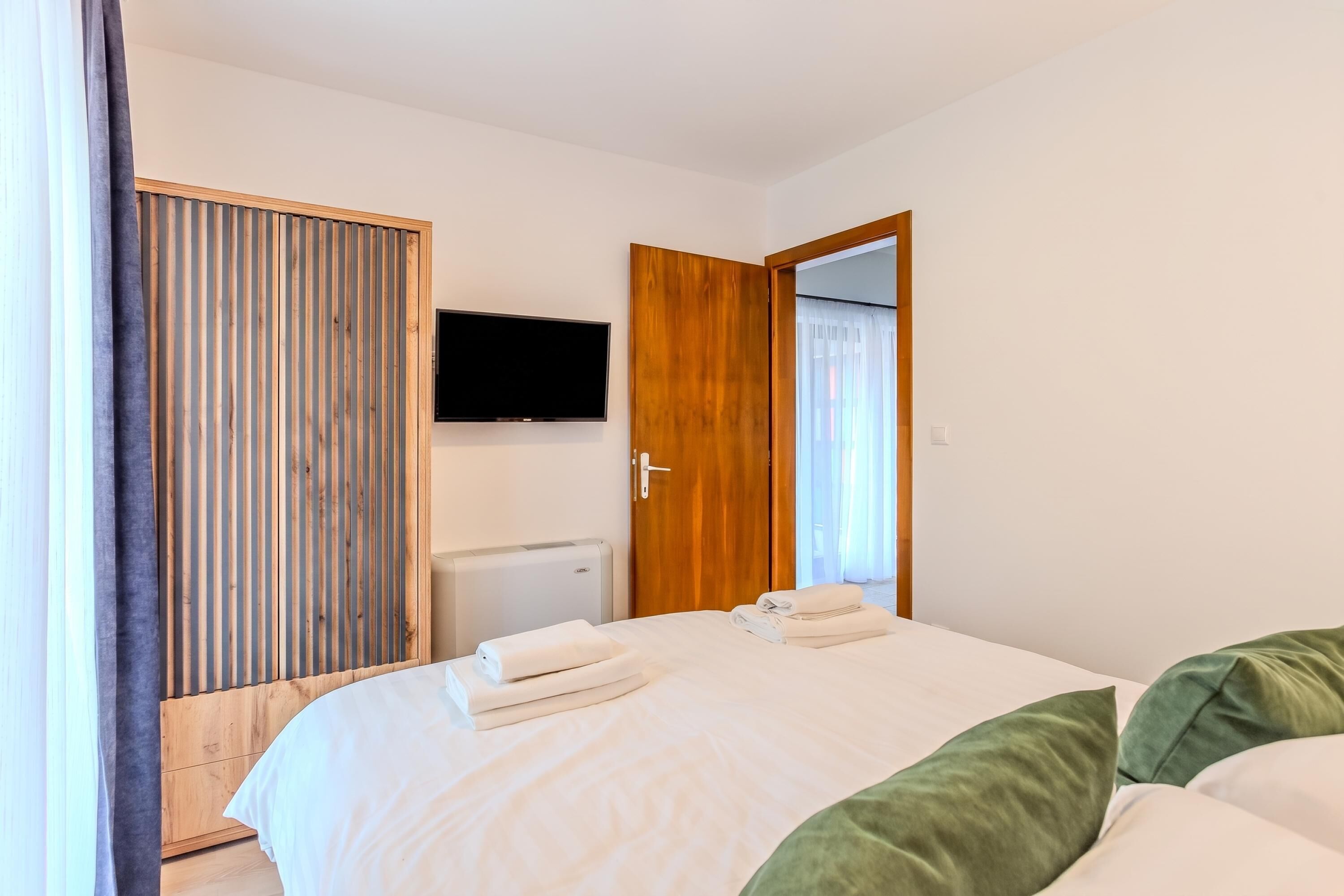 Ein Hotelzimmer mit einem Bett, einem an der Wand befestigten Fernseher, einem Holzschrank und einer Tür, die auf einen Balkon führt.