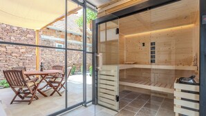 Eine moderne Sauna mit Glastüren, Holzsitzen und einer Wand aus Stein im Hintergrund.
