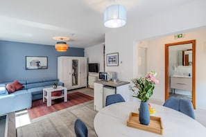 Una moderna camera d'albergo con divano, tavolo da pranzo, angolo cottura e bagno visibile attraverso una porta aperta.