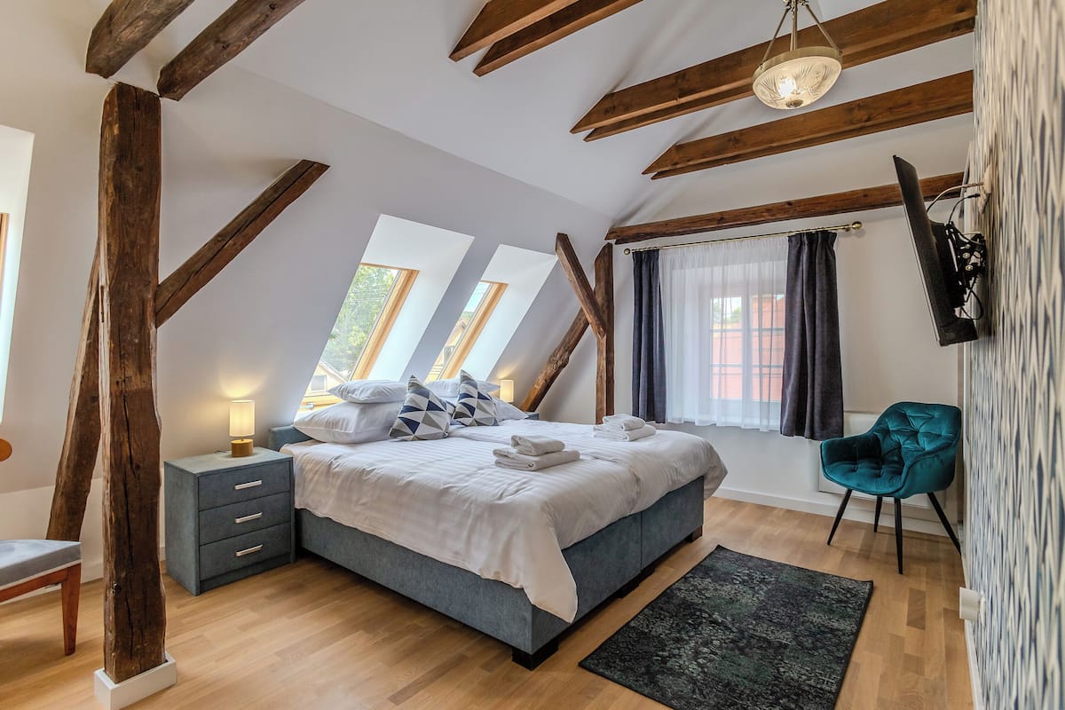 Una camera da letto con un letto, comodini, una sedia, una finestra e una televisione a parete.