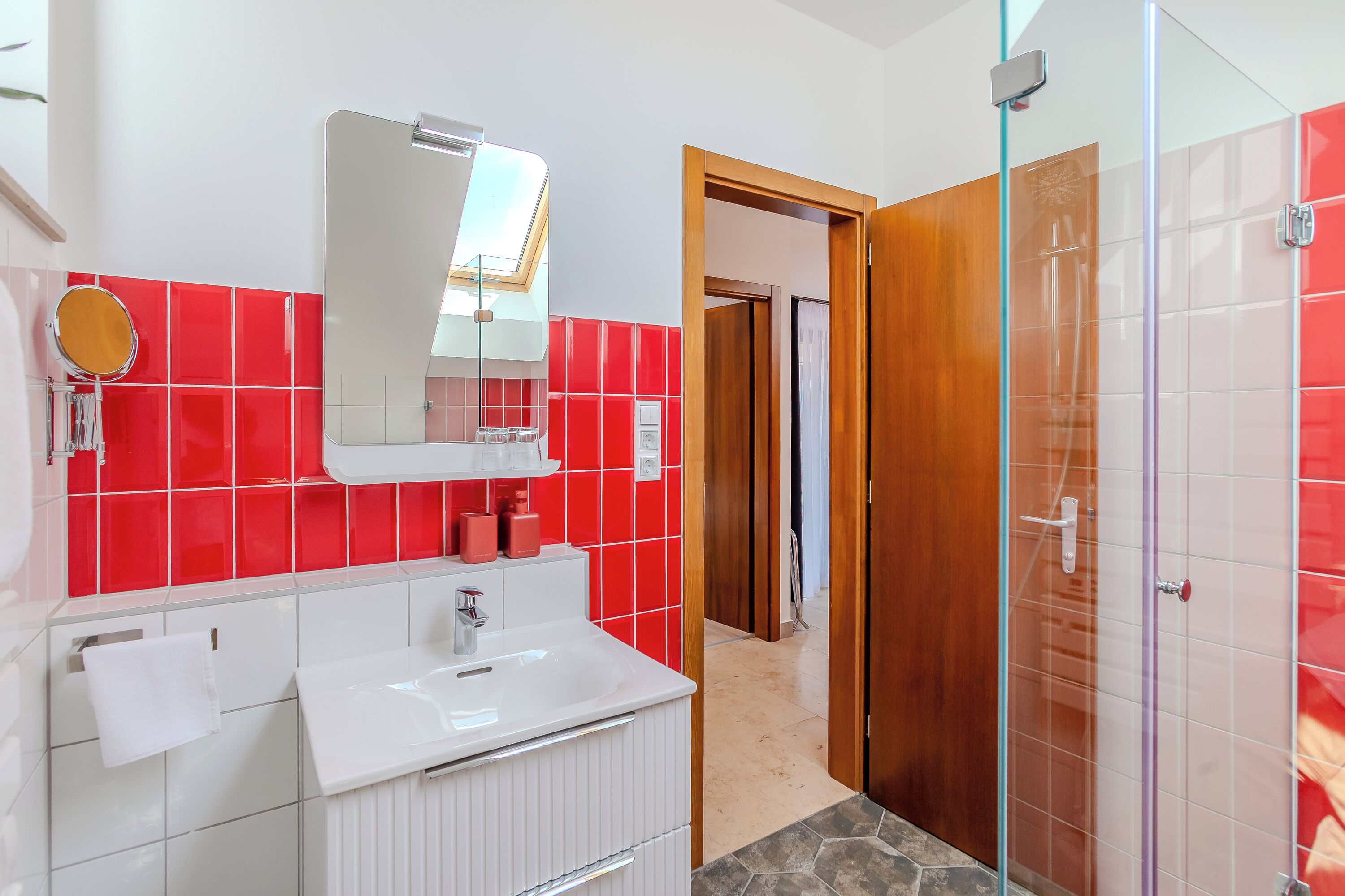 A modern bathroom with a white sink, mirror, and red tiled walls.