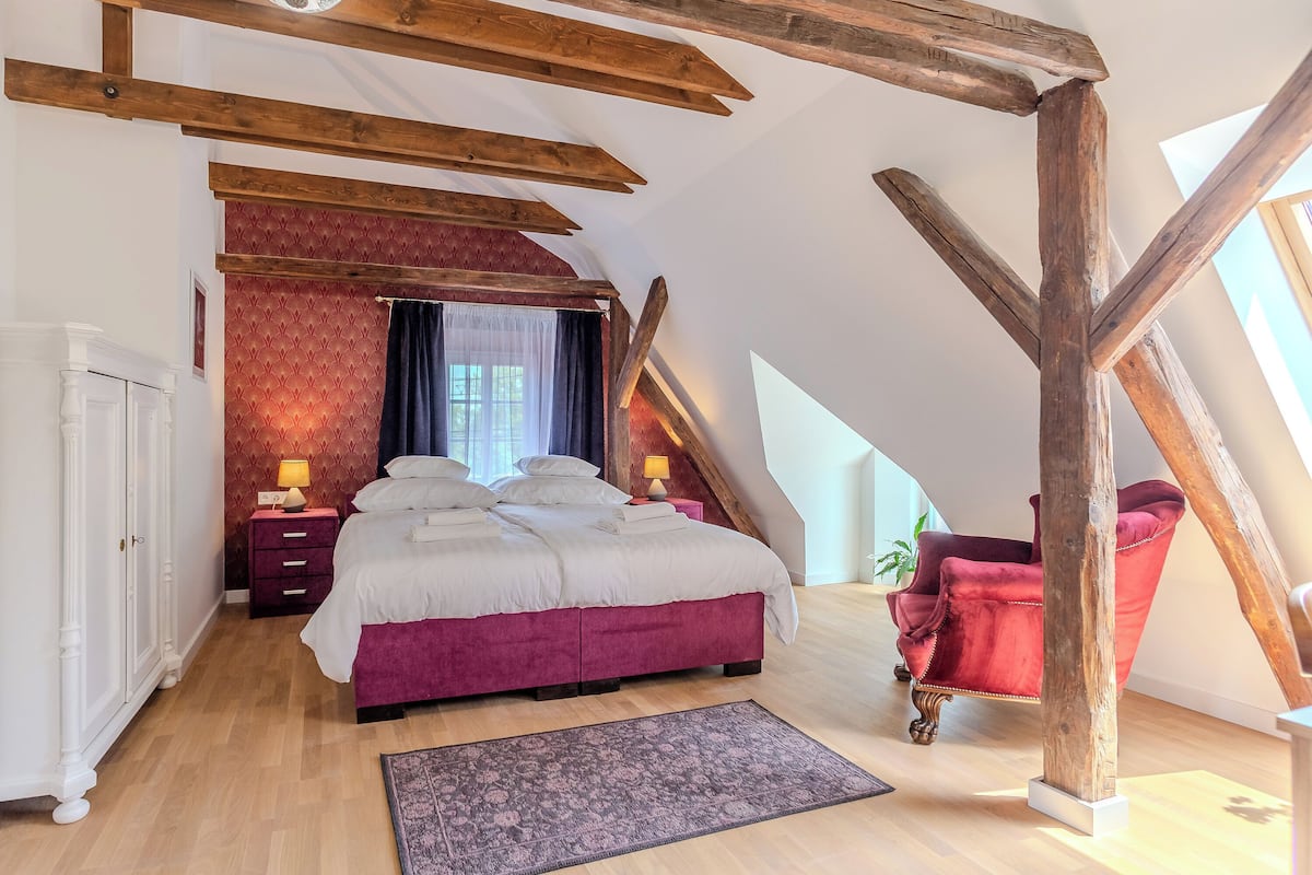 Una camera da letto con un letto grande, una sedia rossa, travi in legno e un muro decorato con motivi rossi.