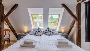 Ein Schlafzimmer mit einem großen Bett, zwei Nachttischen, einem Sessel und Blick durch Dachfenster.