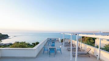 Une terrasse sur le toit offrant une vue sur la mer, avec des espaces de détente en plein air et une pergola.