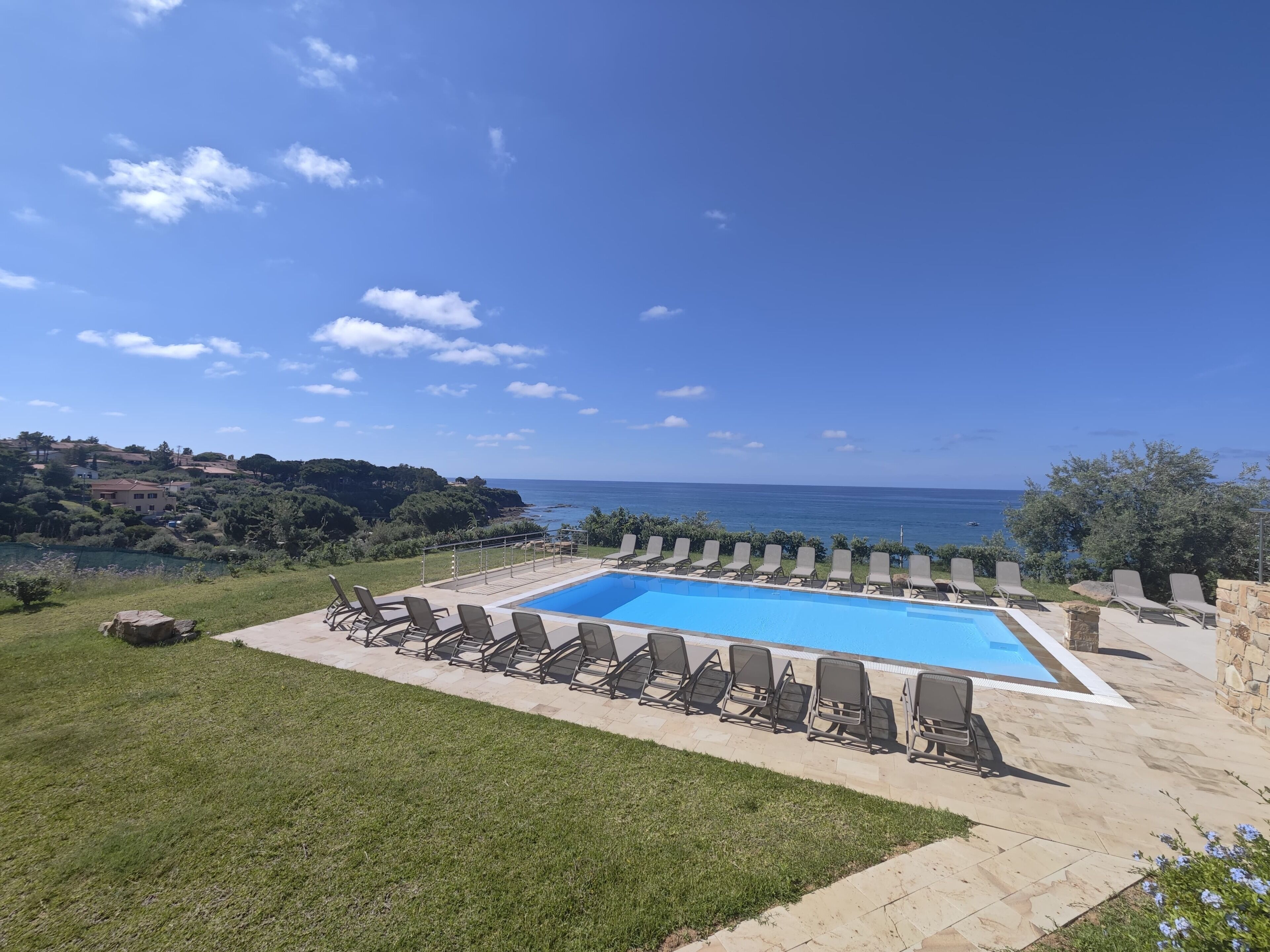 Une piscine rectangulaire entourée de chaises longues, avec en arrière-plan un ciel bleu dégagé et une vue sur la mer.