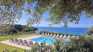 A pool with lounge chairs, surrounded by greenery and overlooking a coastal view.