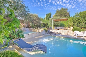 Una piscina amb una banyera d'hidromassatge, gandules i una pèrgola.