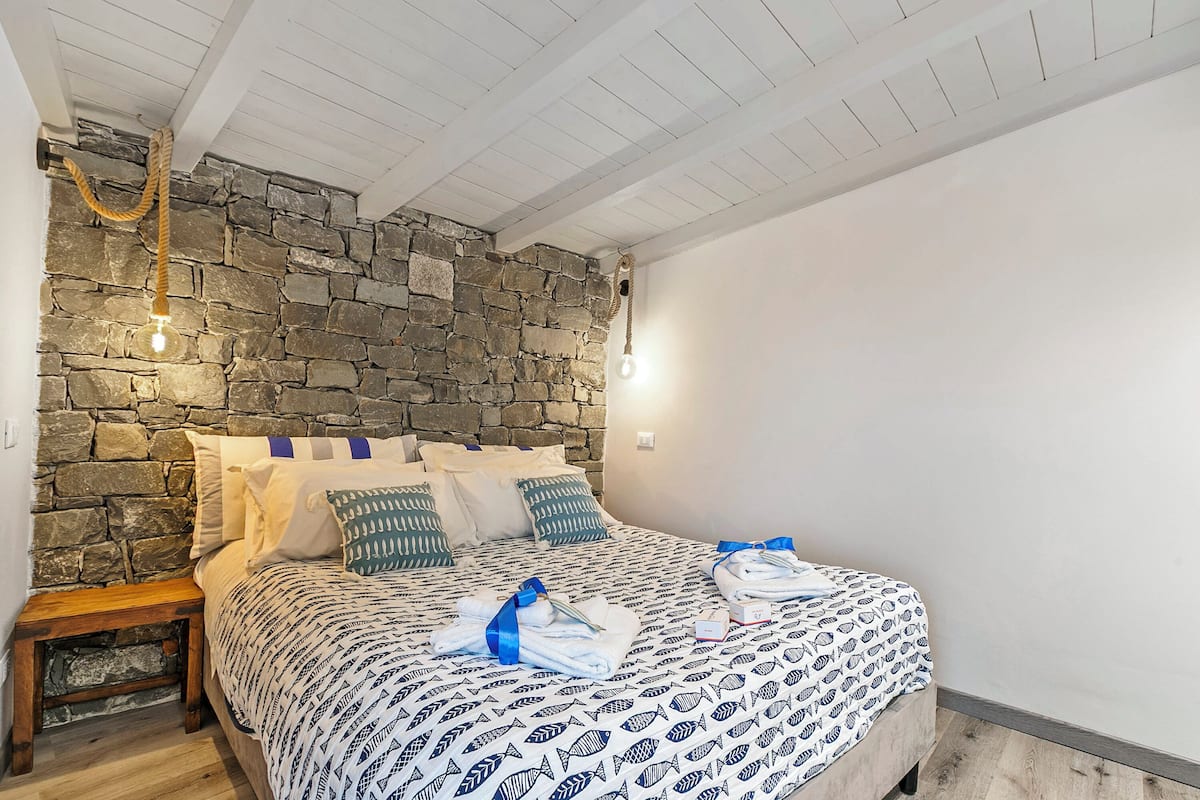 Ein Schlafzimmer mit Steinwand, einem Bett mit gemusterten Betttextilien, einem Nachttisch und einer hängenden Leuchte.