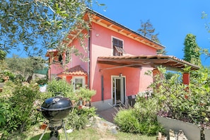 Una casa rosa con un patio, una parrilla y un jardín.