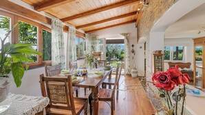 A dining area with wooden tables and chairs, a large window with curtains, and a view of the outdoors. - Casa Fra Gli Ulivi (Ameglia)