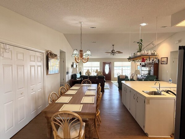 A spacious kitchen with a central island, a dining area with a long table, and a ceiling fan.