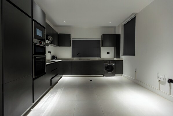 Una cocina moderna con electrodomésticos integrados, lavadora y un ventanal amplio.