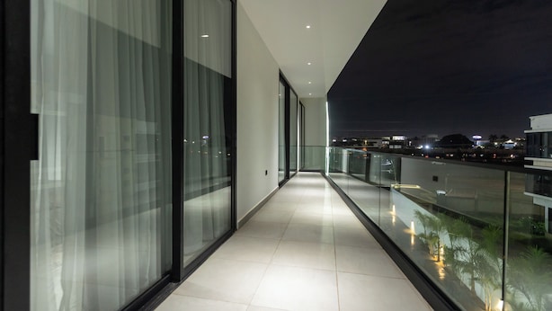 Un pasillo moderno con paredes de vidrio y un balcón con vistas a un paisaje urbano nocturno.