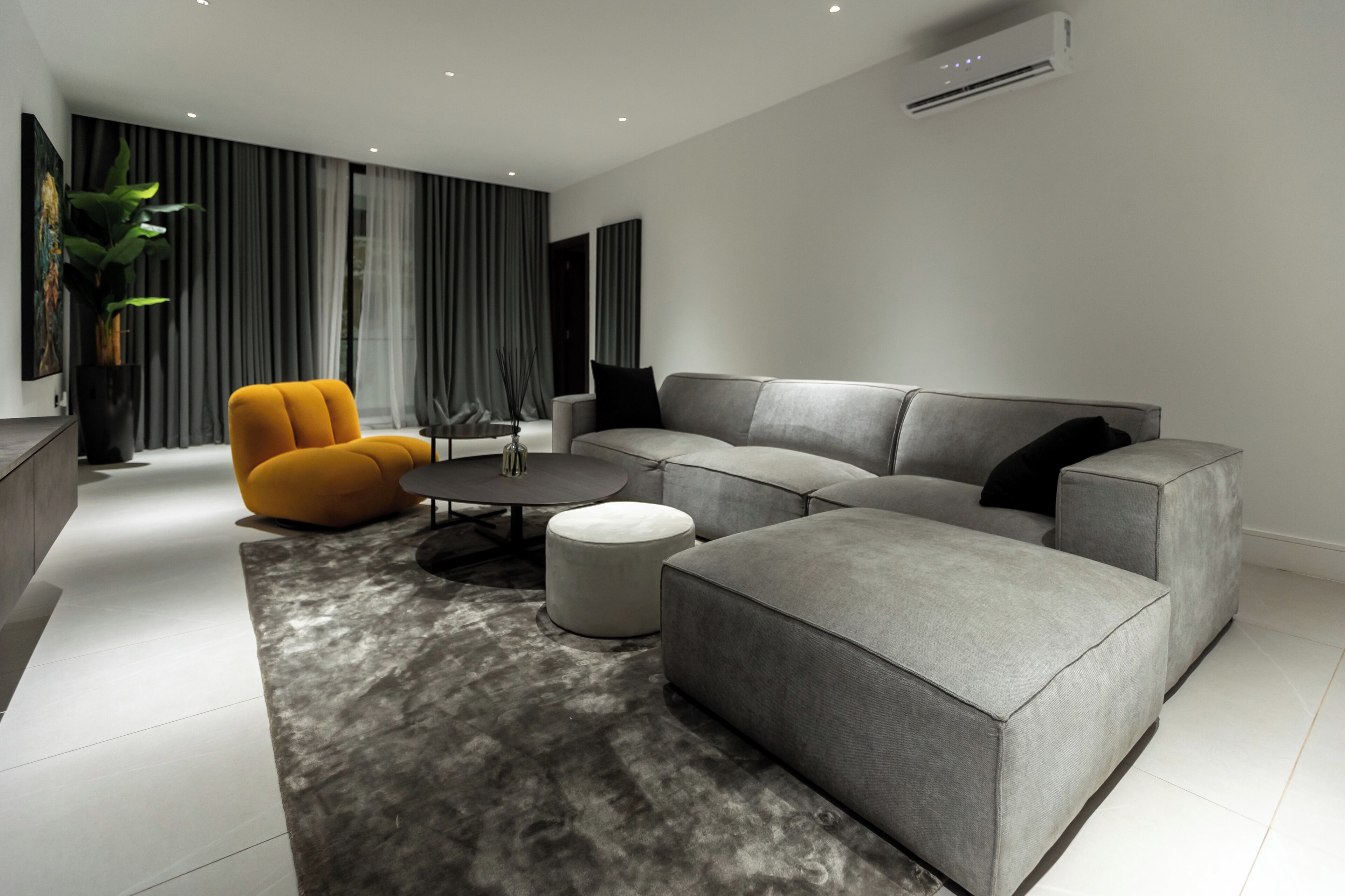 A modern living room with a grey sectional sofa, a yellow armchair, and a round coffee table.