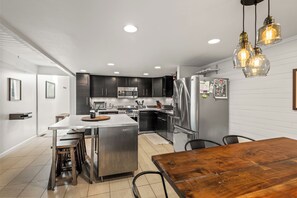 A modern kitchen with stainless steel appliances, a wooden dining table, and pendant lighting.