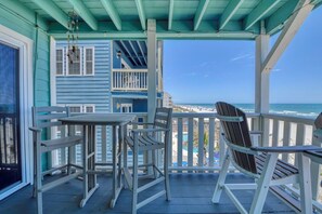 Un porche cubierto con una mesa y sillas, con vista a una playa y una piscina.