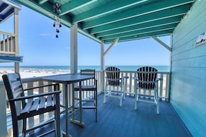 Una terraza techada con una mesa y sillas, con vistas a la playa.