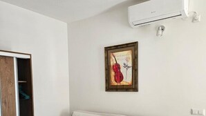Un salon moderne avec un canapé, un tableau encadré représentant un violon et un appareil de climatisation.