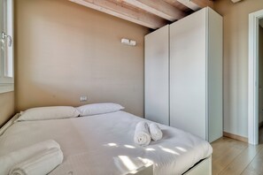 A bedroom with a bed, two rolled towels, a wardrobe, and a door leading to another room.