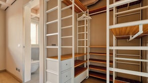 Un dressing accessible sans porte, doté d’étagères et de tiroirs ouverts, d’un plancher en bois et d’une fenêtre avec des stores.