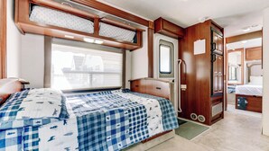 A compact RV interior with a bed, kitchenette, and a small bathroom. - Custom Motorhome that brings joy. (Ann Arbor)