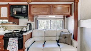 A compact RV kitchen with a microwave, stove, and seating area. - Custom Motorhome that brings joy. (Ann Arbor)