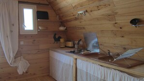 A wooden cabin kitchen with a window, a sink, a stove, and a hanging basket.