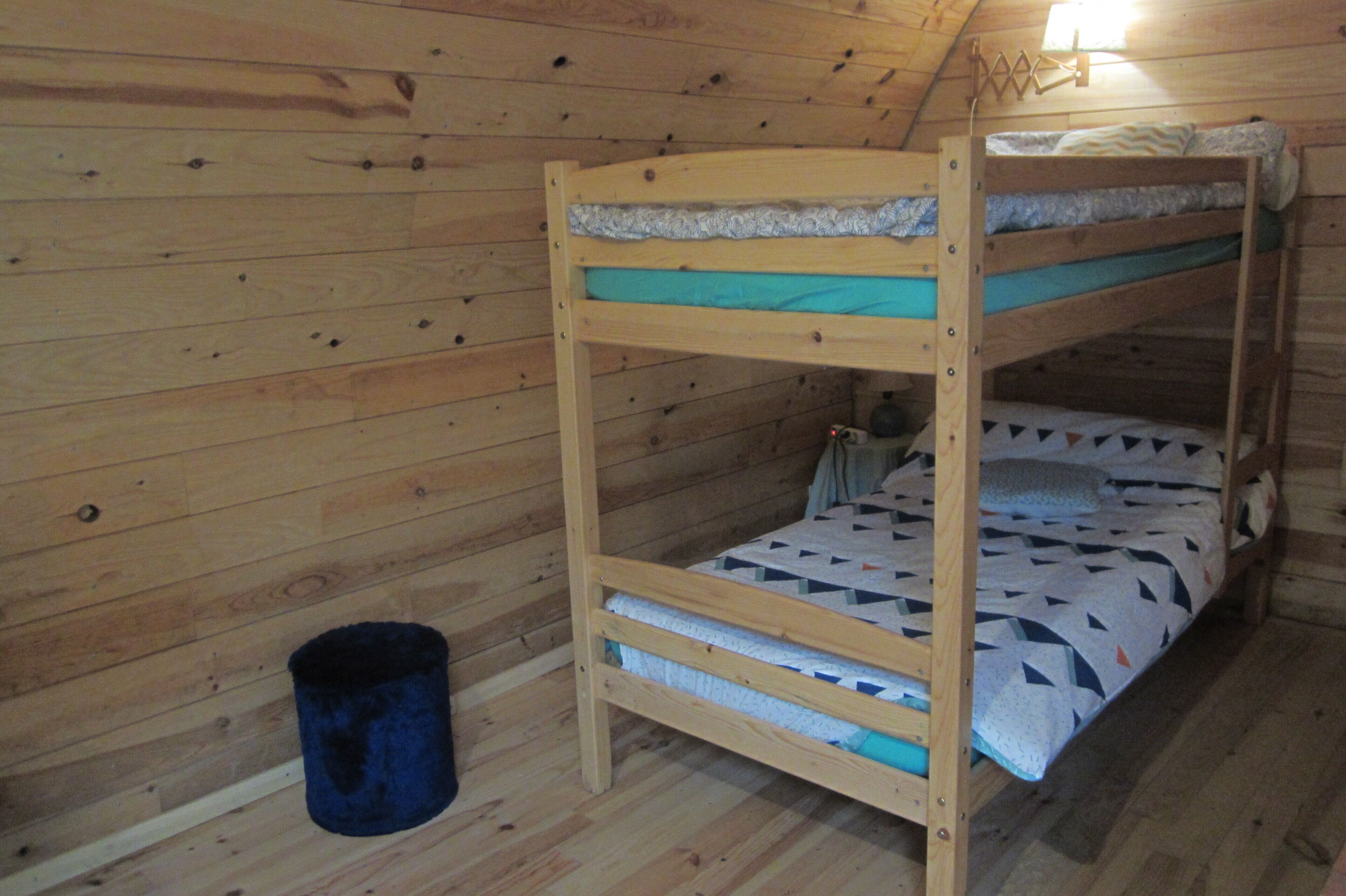 A bunk bed room with wooden walls and a single trash bin.