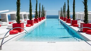 A pool area with red and white seating, a clear blue pool, and a view of the ocean.