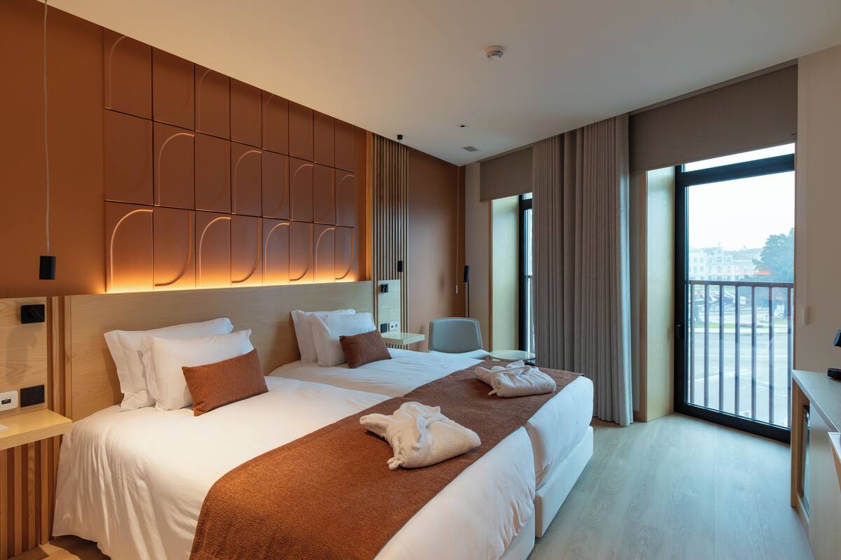 A hotel room with a large bed, a desk, and a view of the city through the window.